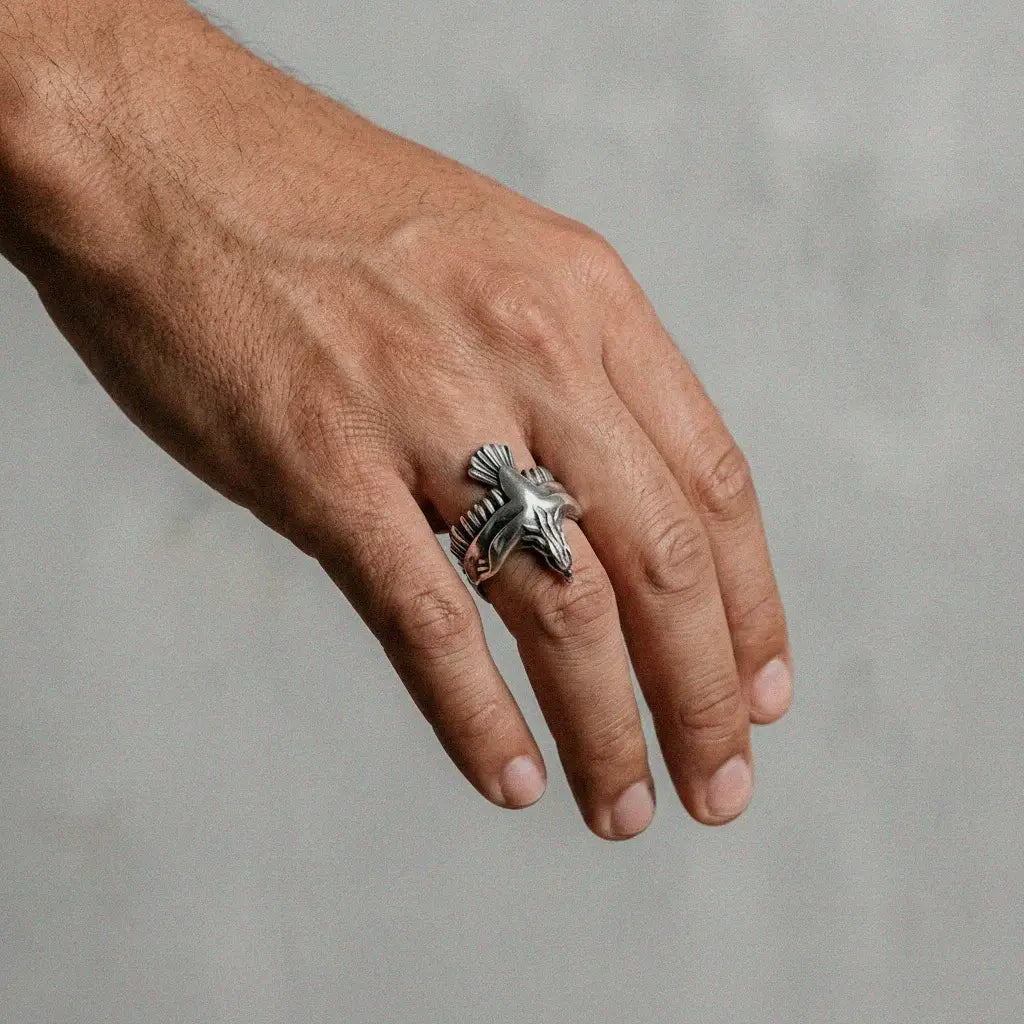 Hand wearing a silver ring with an eagle design on a neutral background