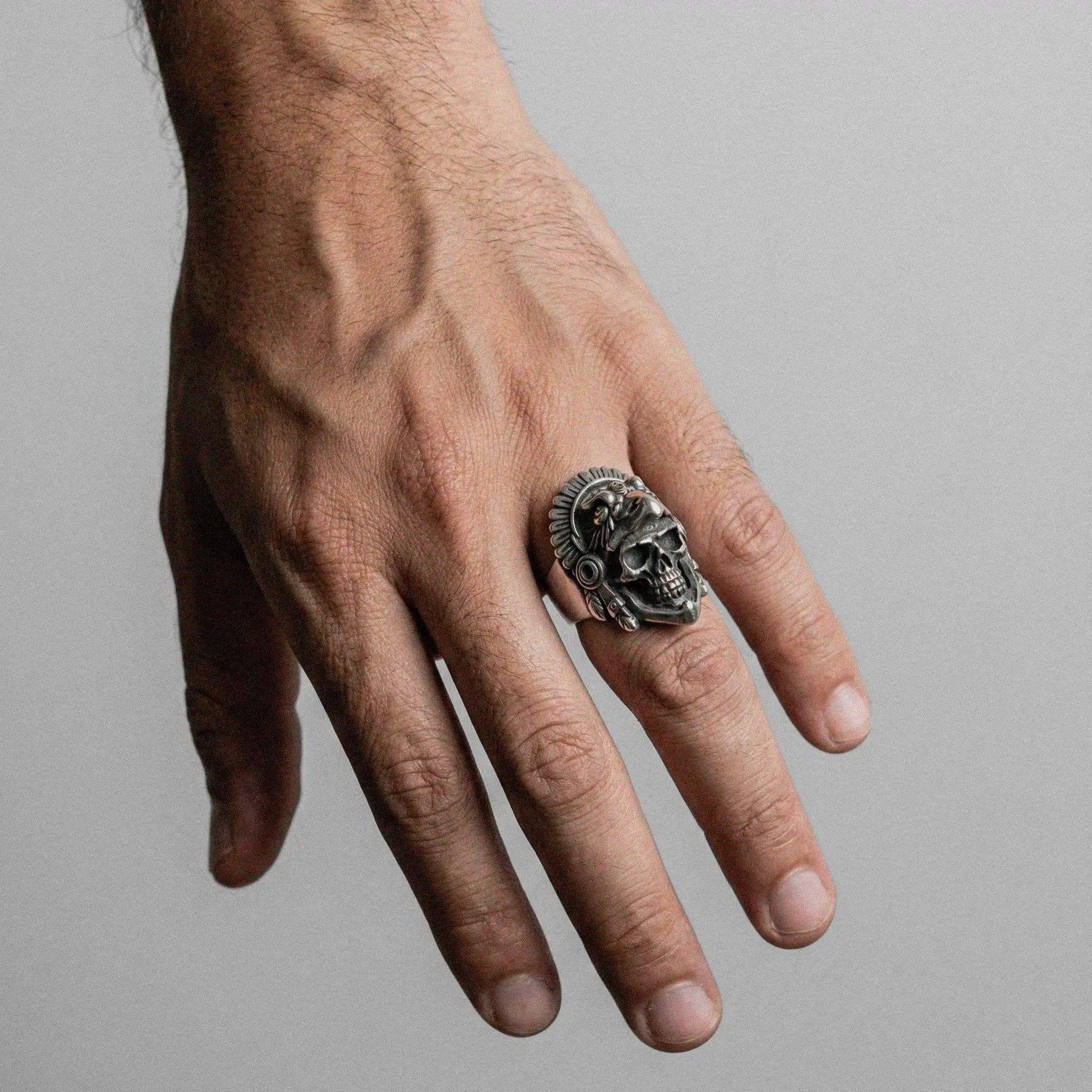 Hand wearing a eagle-warrior skull ring on a plain background