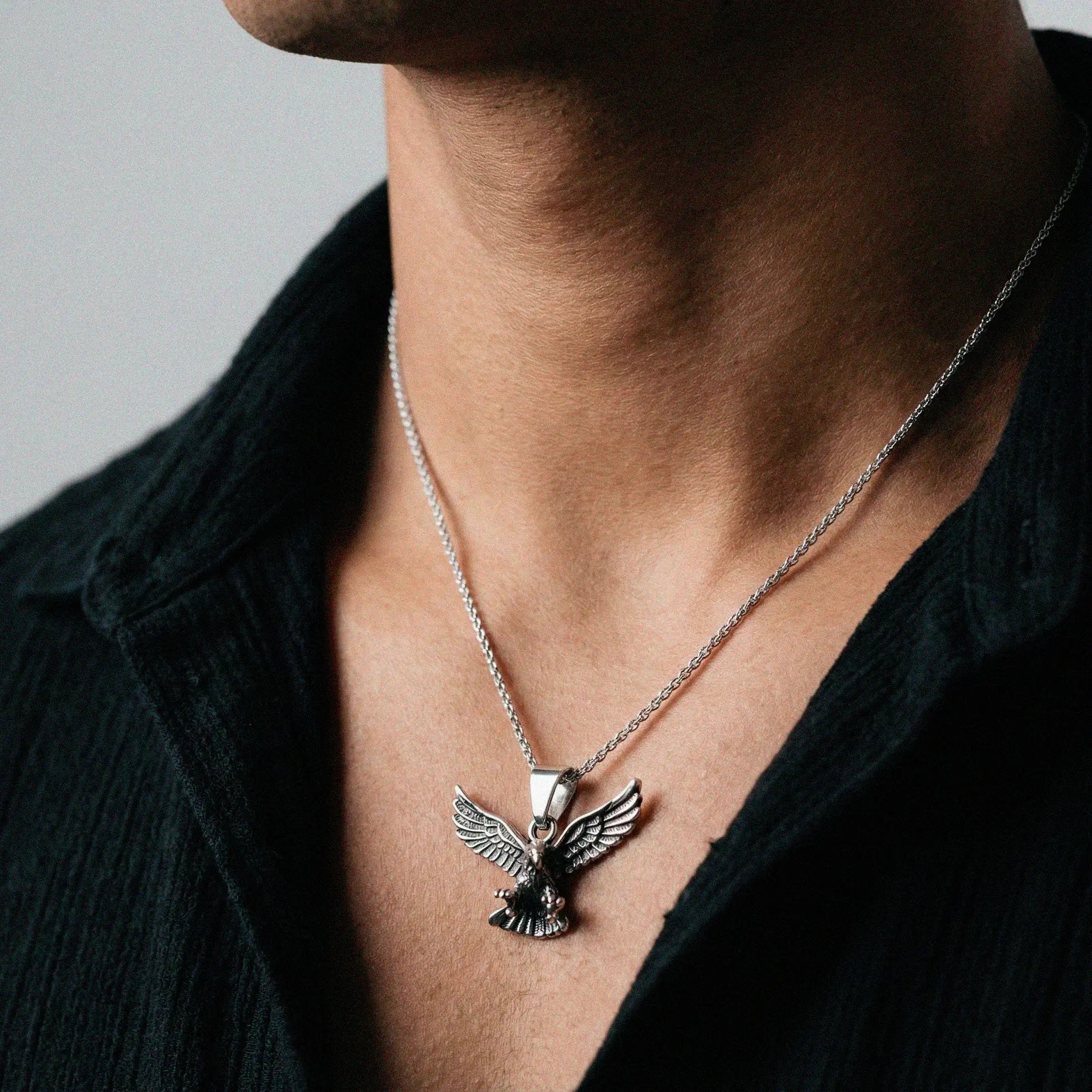 Silver eagle pendant necklace on a person wearing a black shirt against a neutral background