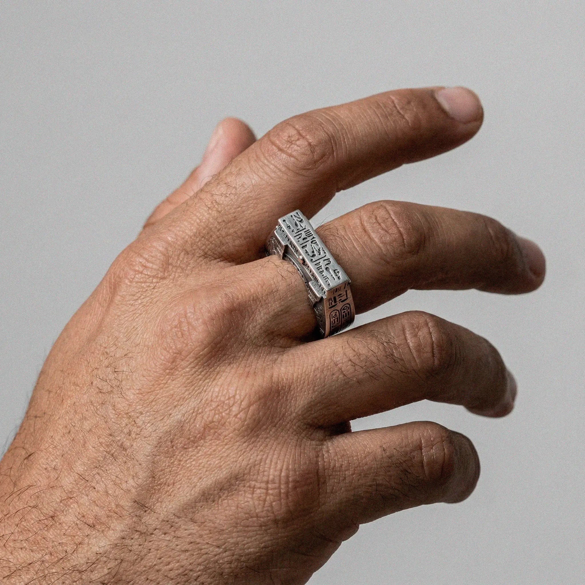 Hand wearing a silver ring with egyptian text on a gray background