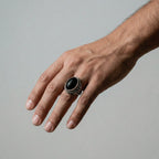Hand wearing a silver ring with a black stone on a gray background