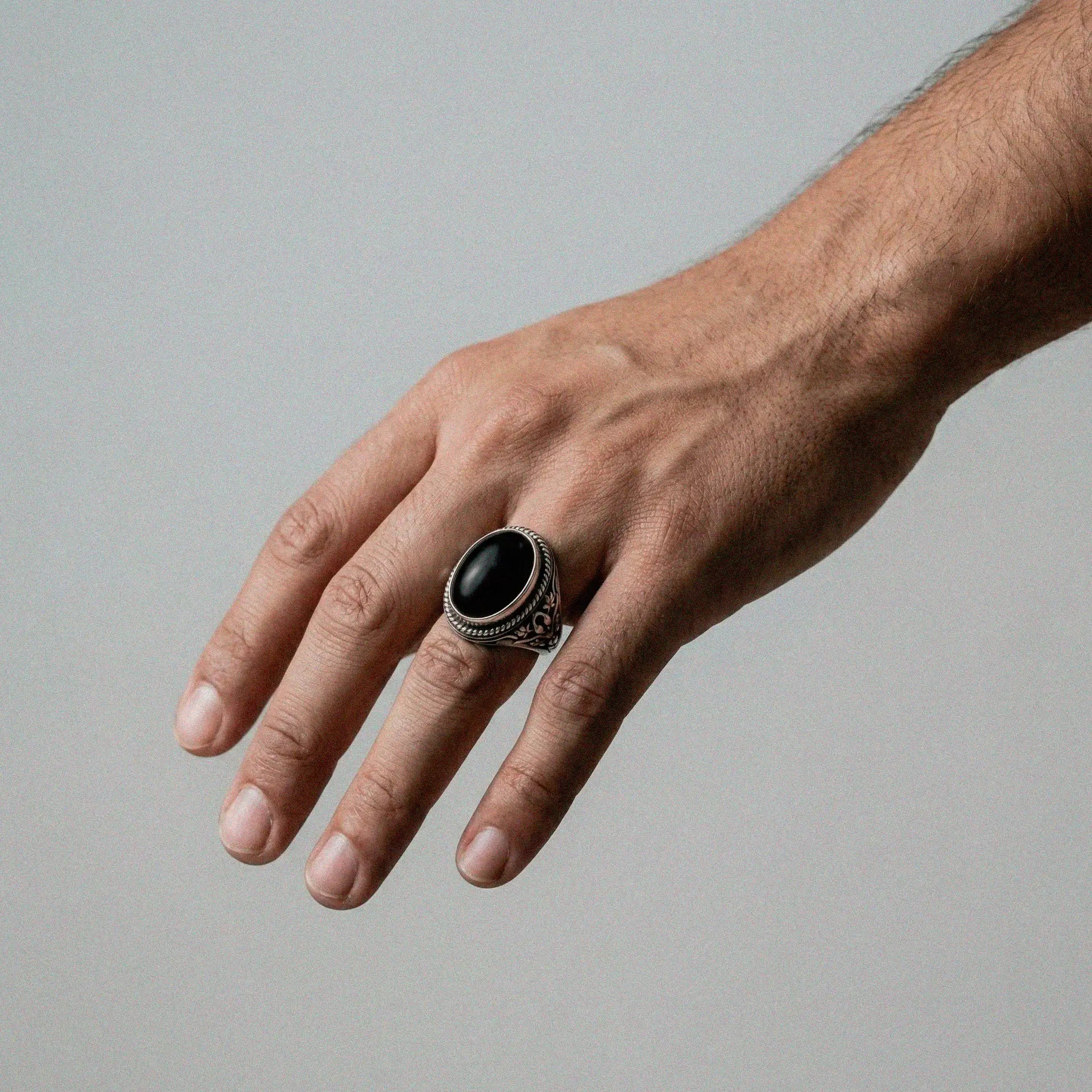 Hand wearing a silver ring with a black stone on a gray background