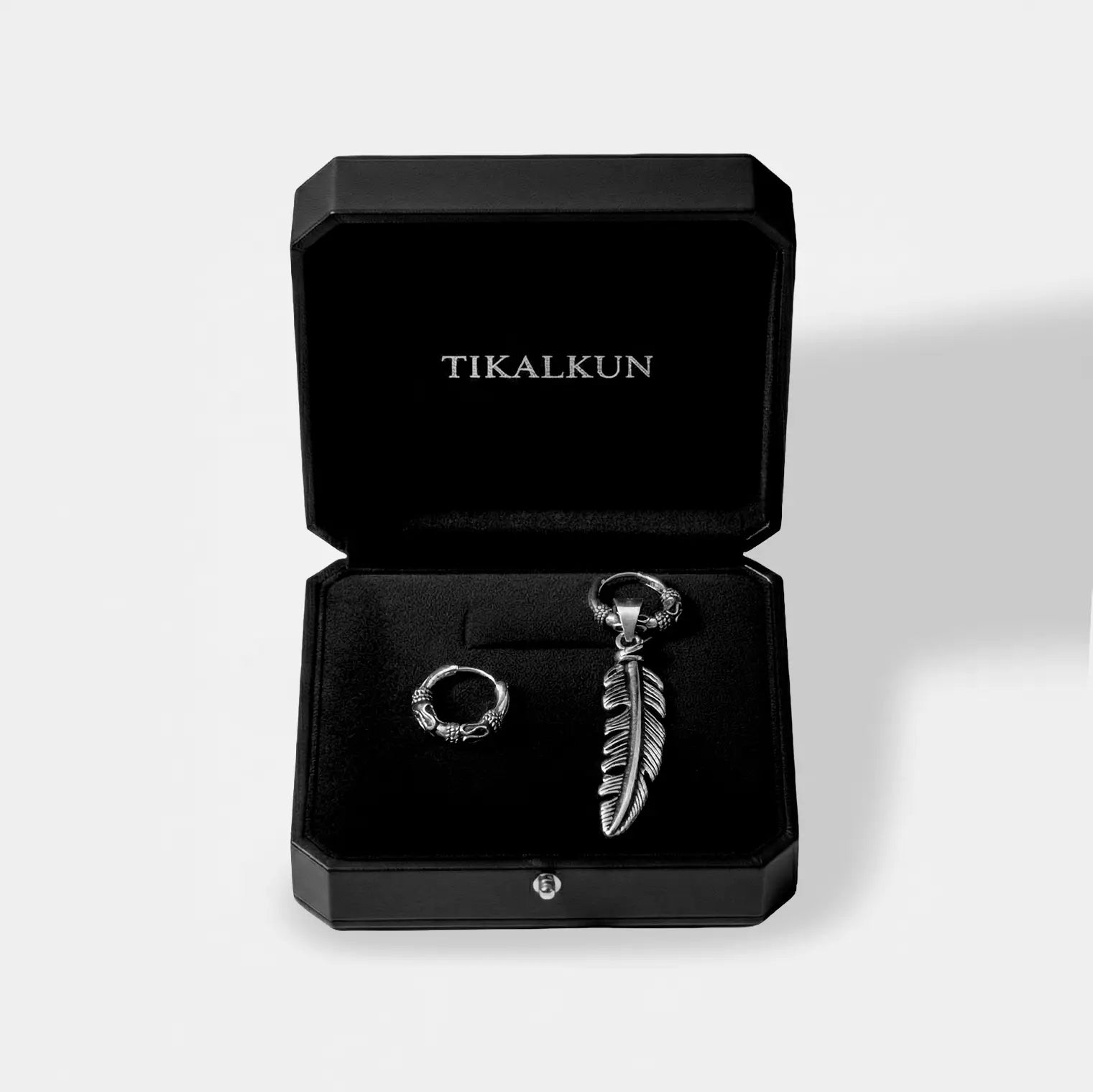 Silver earring with feather design in a black Tikalkun box on a light gray background