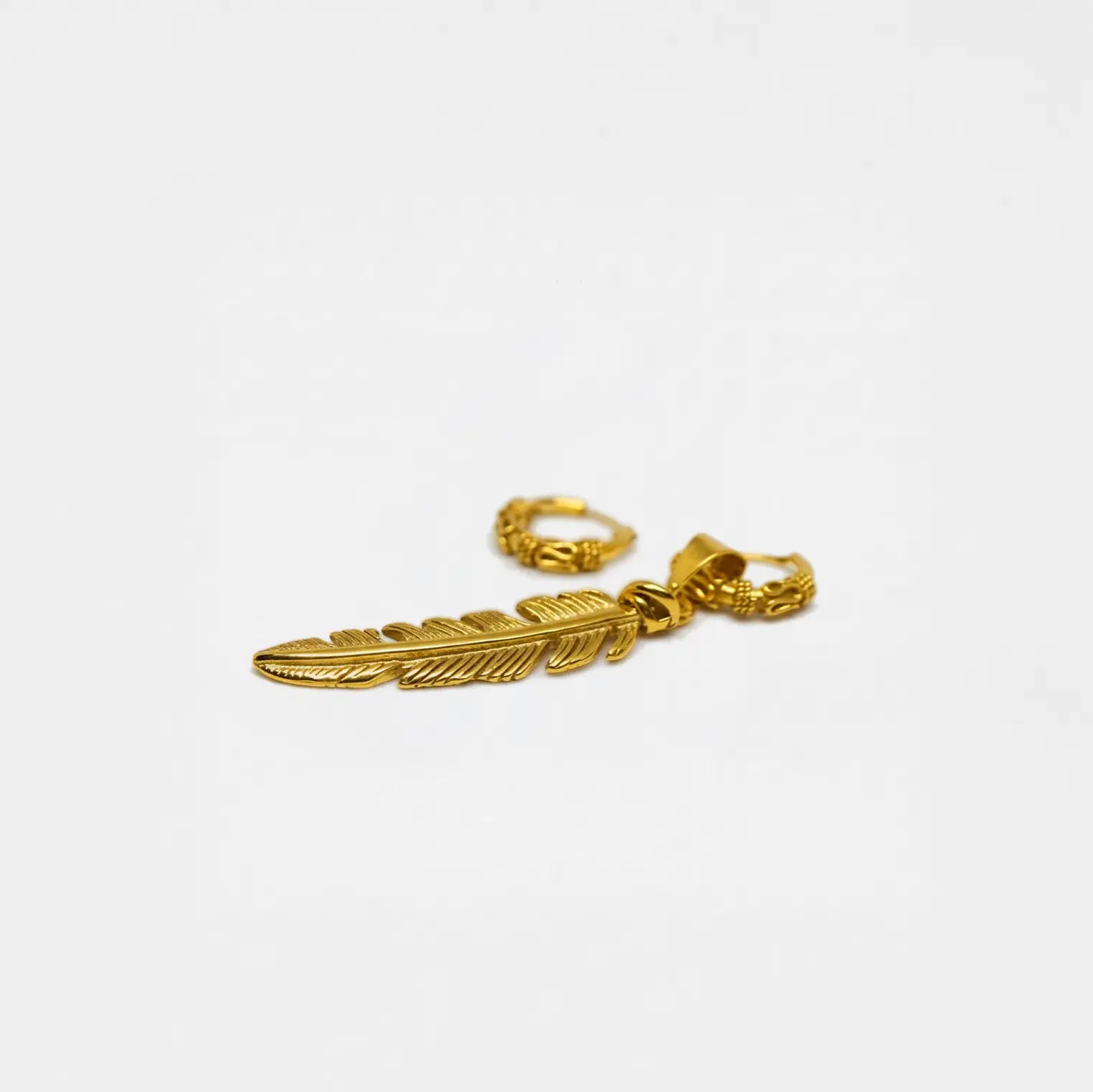 Gold feather-shaped earring on a white background