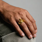 Hand wearing a gold fire-flame ring on a gray background
