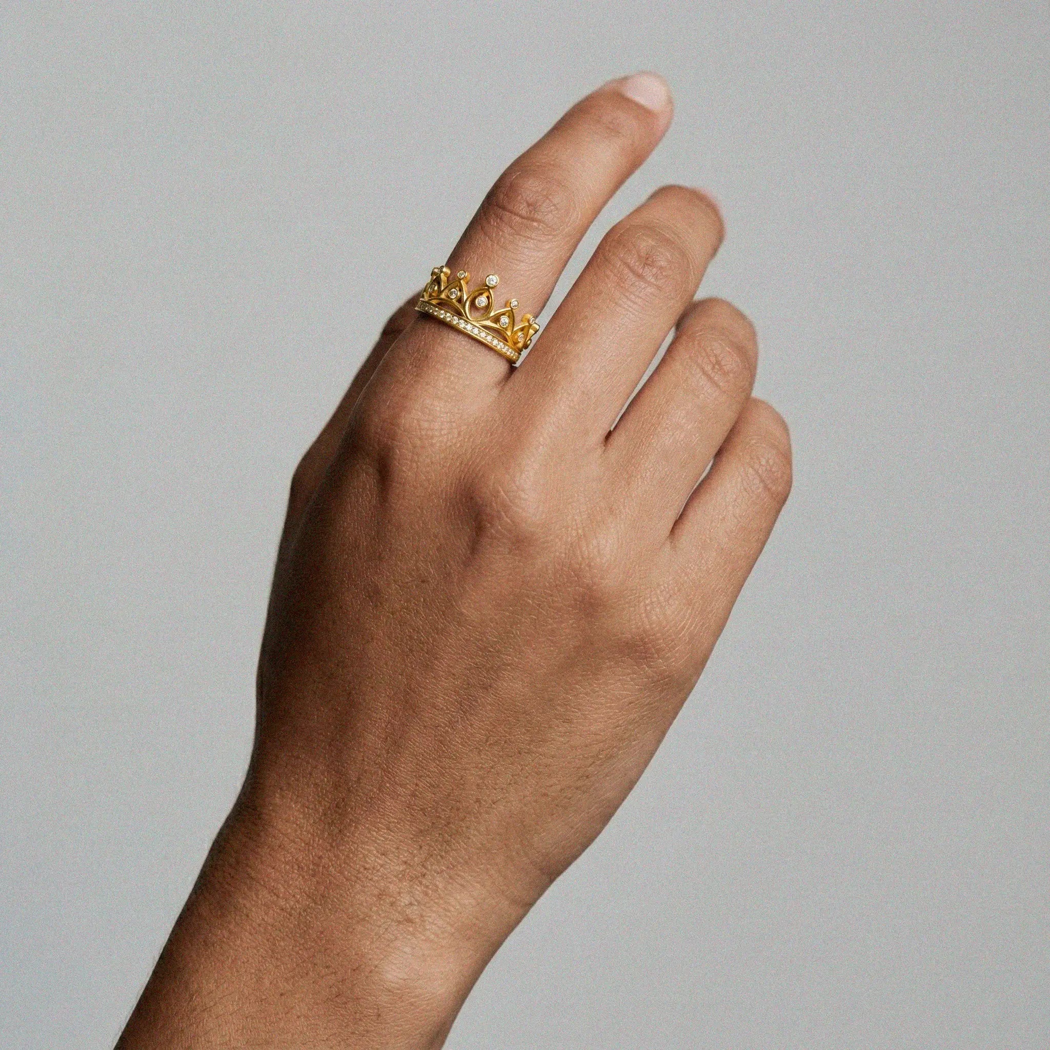 Hand wearing a gold ring with a crown design on a plain background