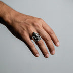 Hand wearing a silver ganesha ring on a plain background