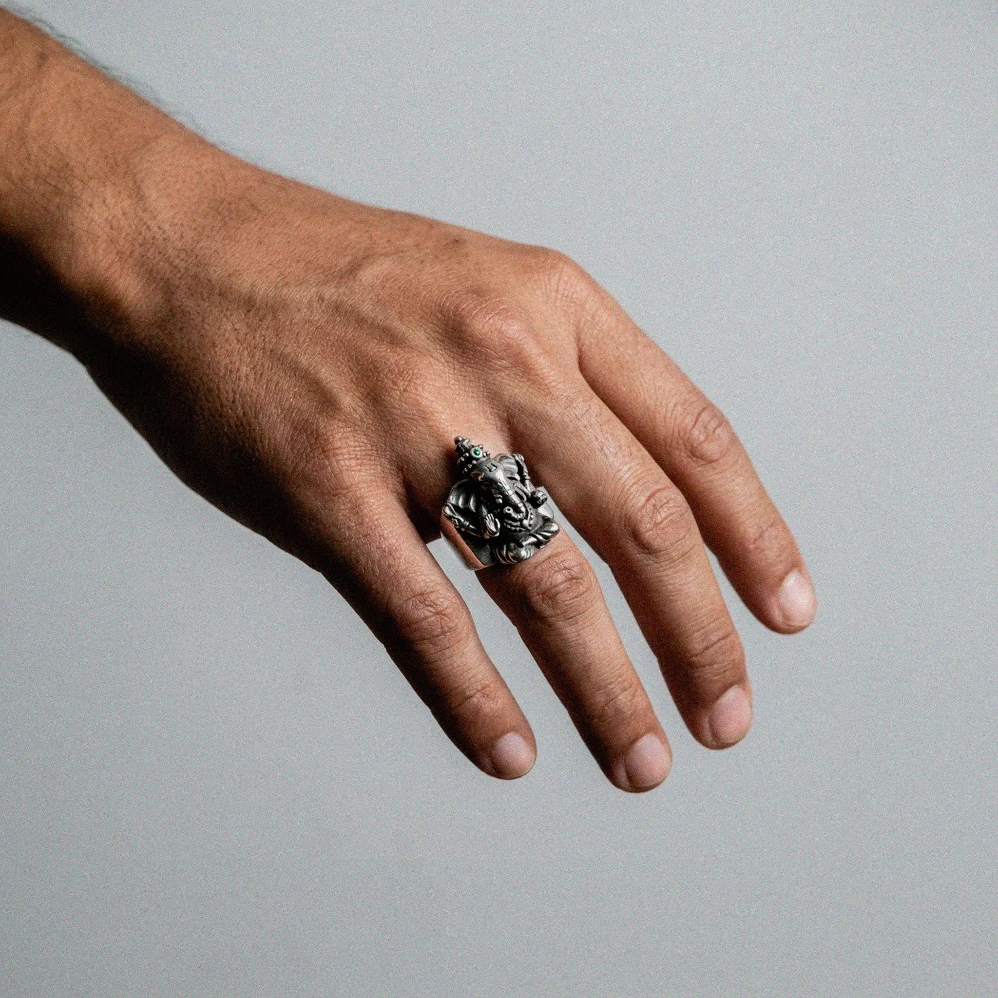 Hand wearing a silver ganesha ring on a plain background
