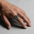 Hand wearing a buddha silver ring with a face design on a gray background