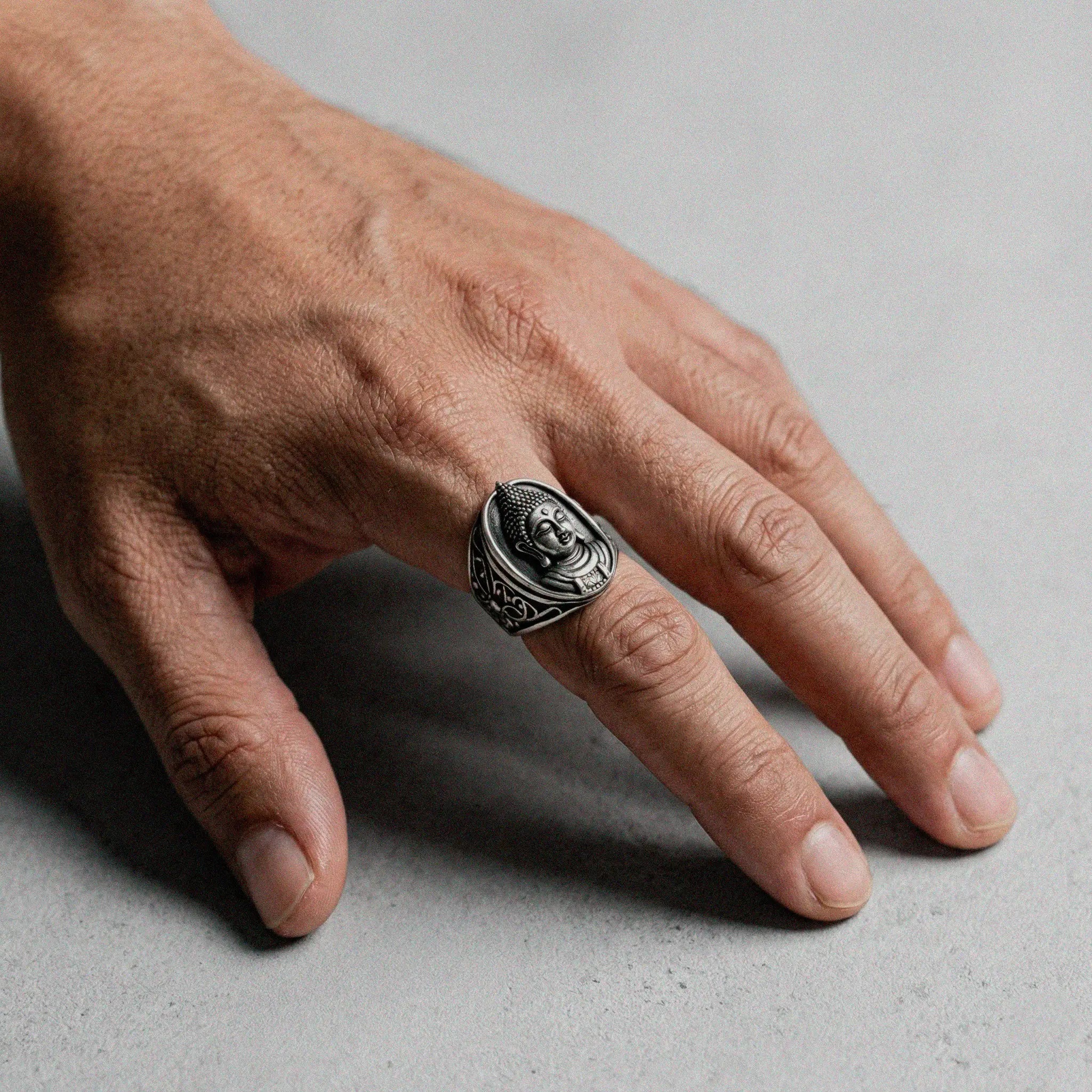 Hand wearing a buddha silver ring with a face design on a gray background