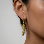 Gold feather earring worn by a person with a neutral background