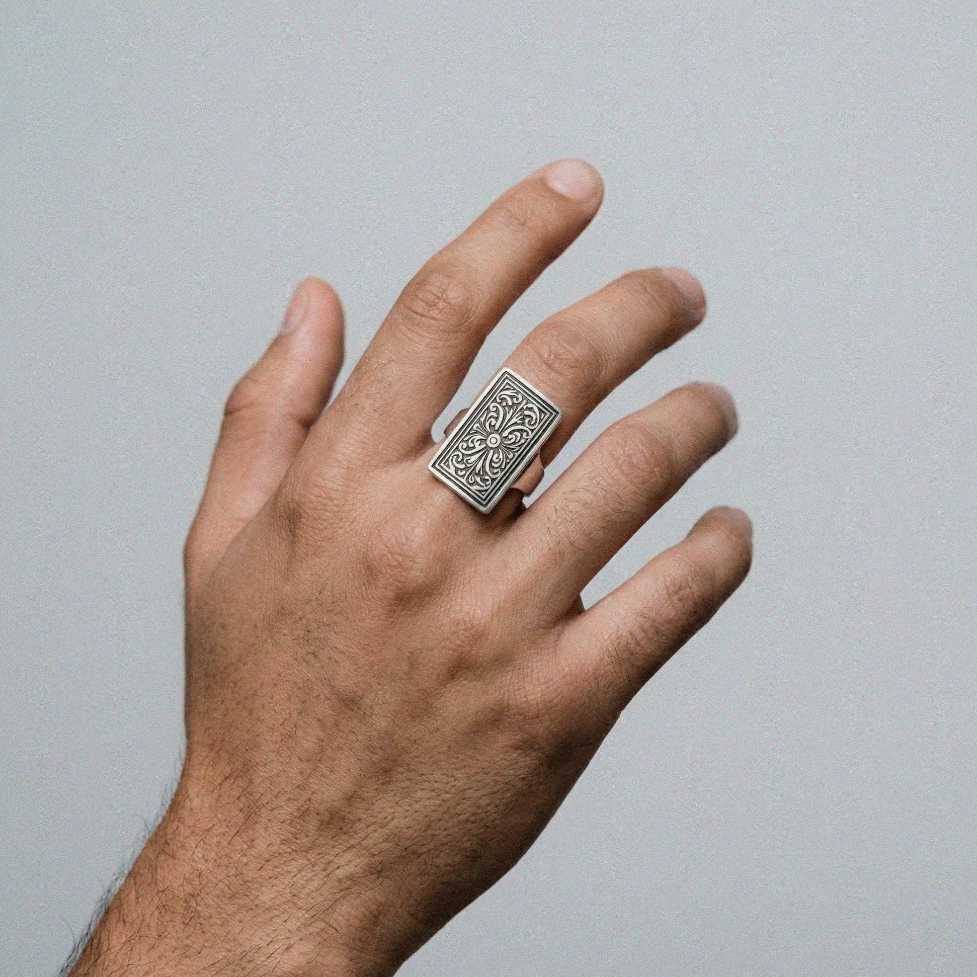 man's hand wearing  a silvr mexican ring on a gray background