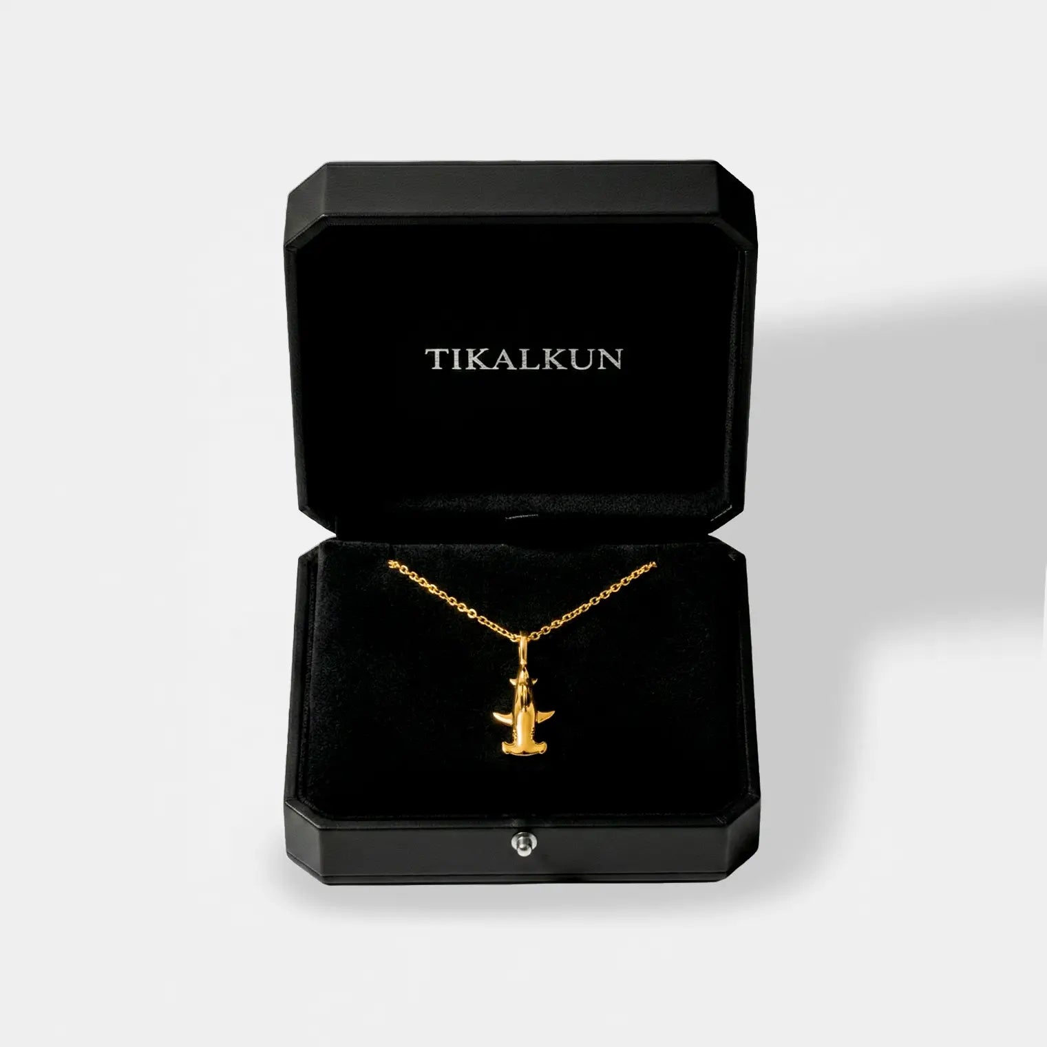 Gold hammerhead-shark necklace in a black Tikalkun jewelry box on a light gray background