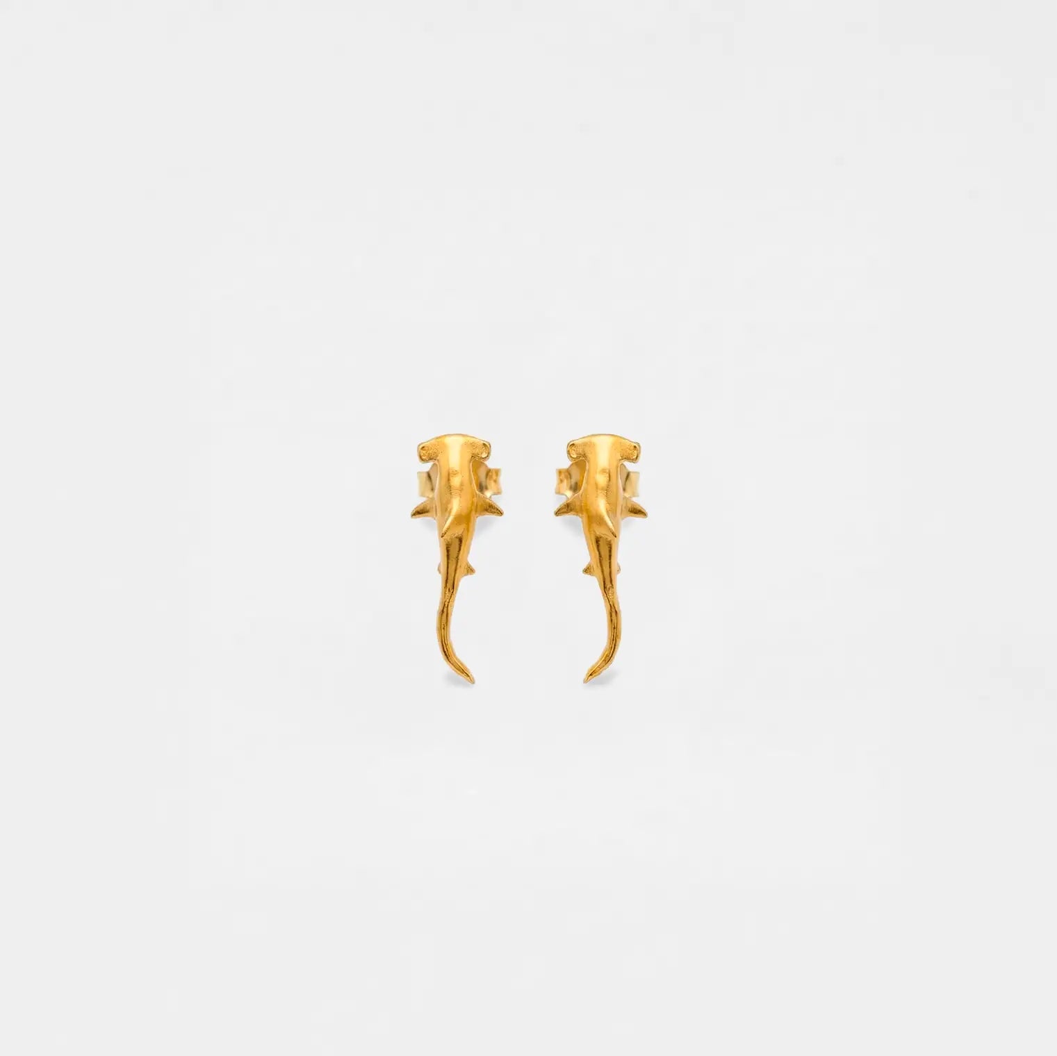 Pair of gold hammerhead-shark earrings on a light gray background