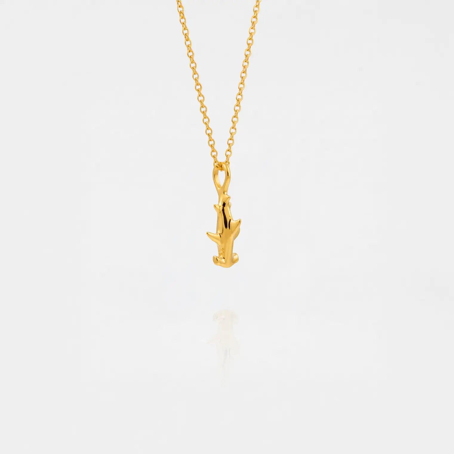 Gold necklace with a small hammerhead-shark pendant on a light gray background