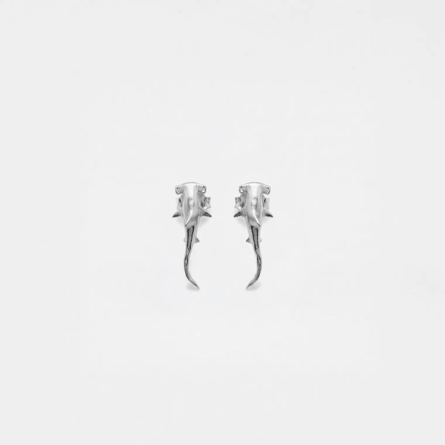 Pair of silver  hammerhead-shark earrings on a light gray background