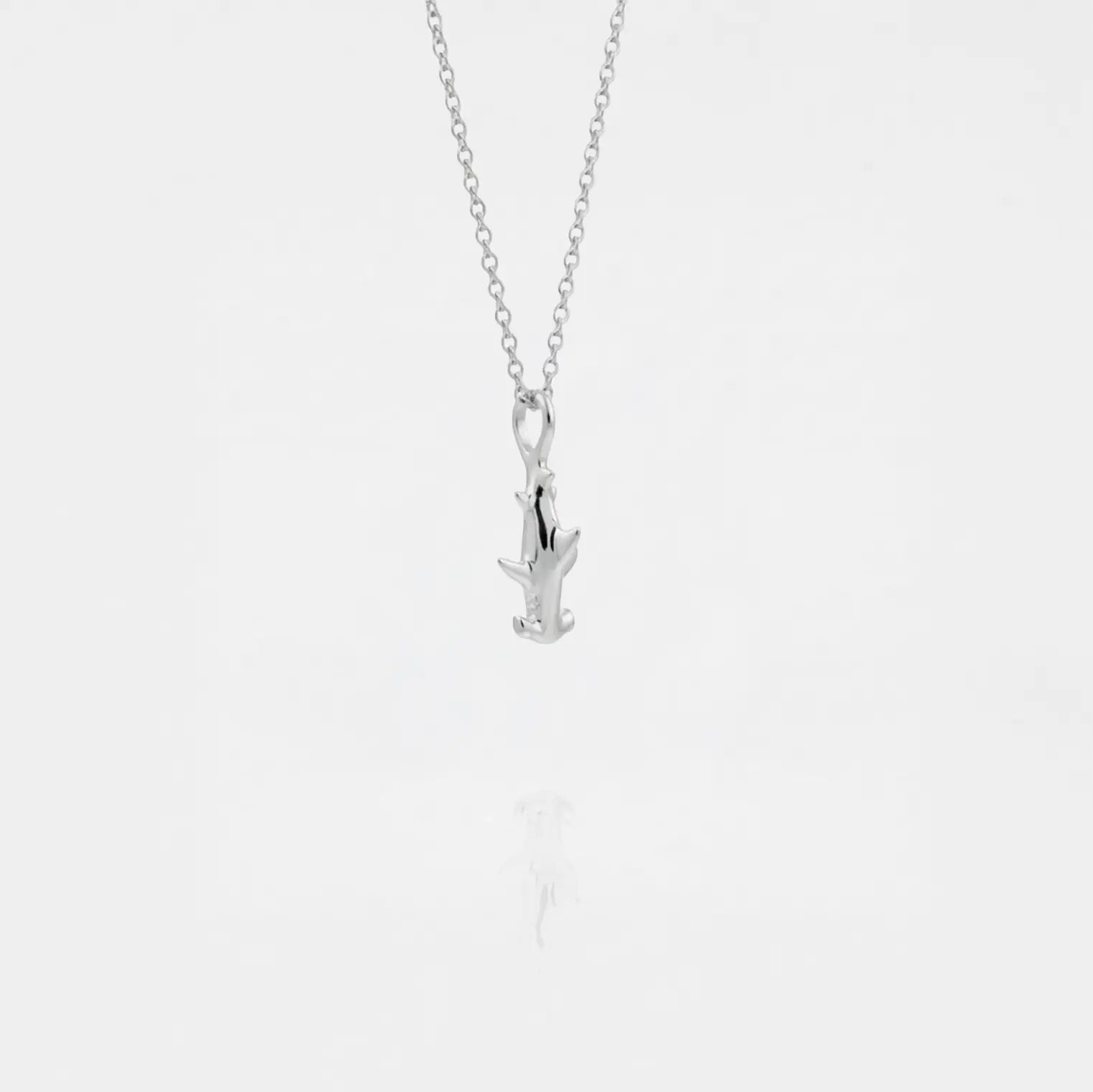 Silver necklace with a small hammerhead-shark pendant on a light gray background