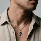 Man wearing a beige shirt with a necklace featuring an hamsa handpendant.