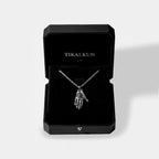 Black jewelry box with 'TIKALKUN' branding containing a necklace with a hamsa hand pendant.