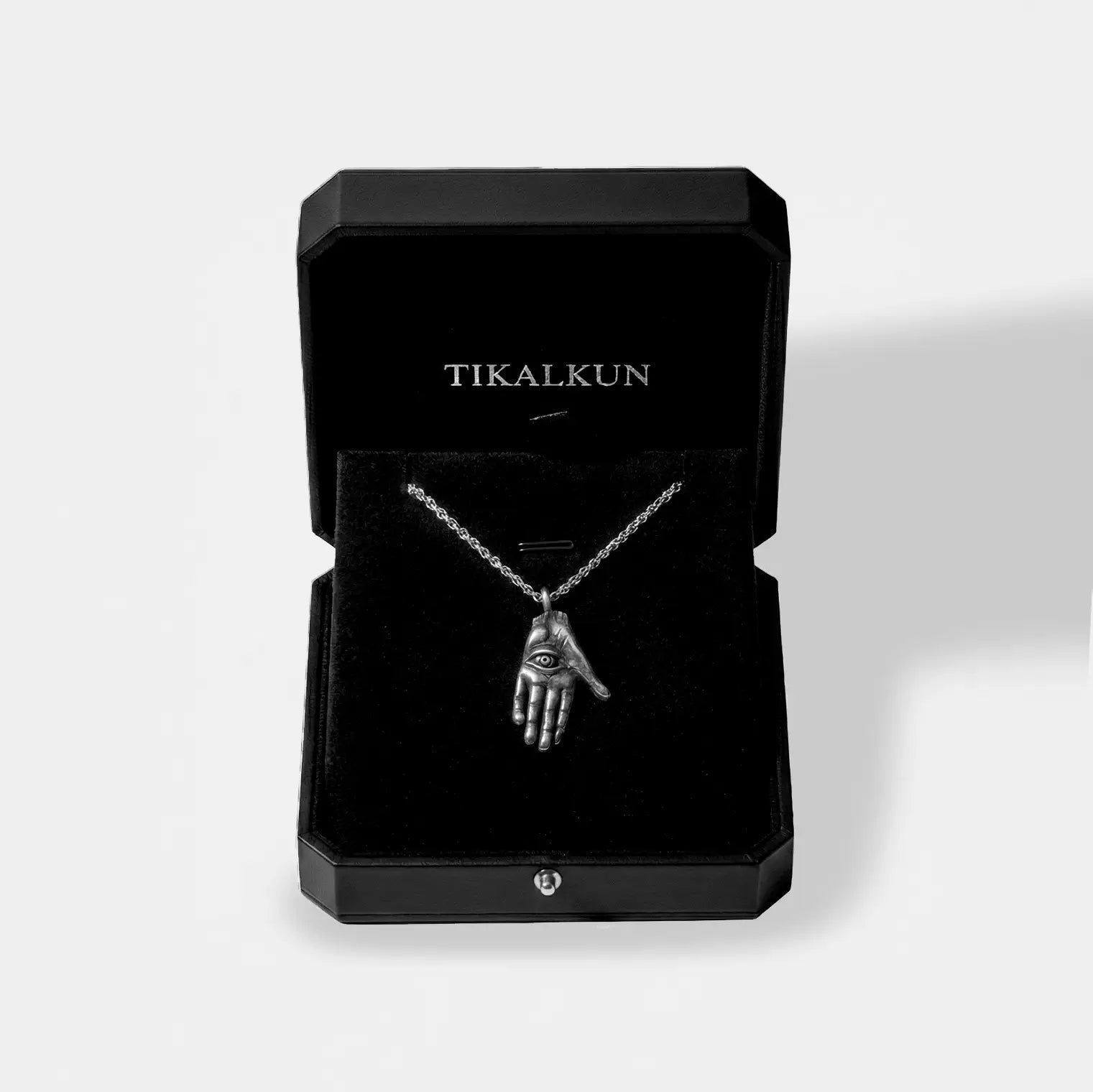 Black jewelry box with 'TIKALKUN' branding containing a necklace with a hamsa hand pendant.