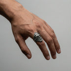 Hand wearing a silver ring with a knight's helmet design on a gray background