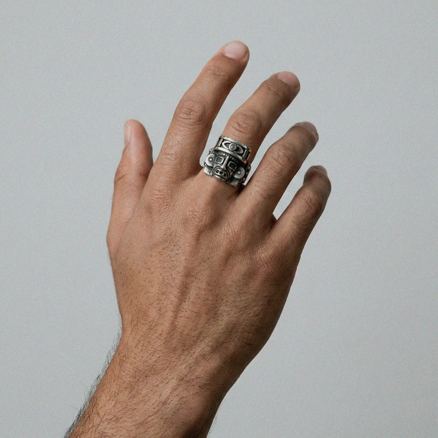 Hand wearing an aztec god silver ring on a plain background
