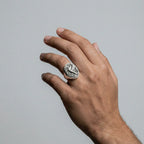 Hand wearing a silver ring with a hummingbird design on a plain background