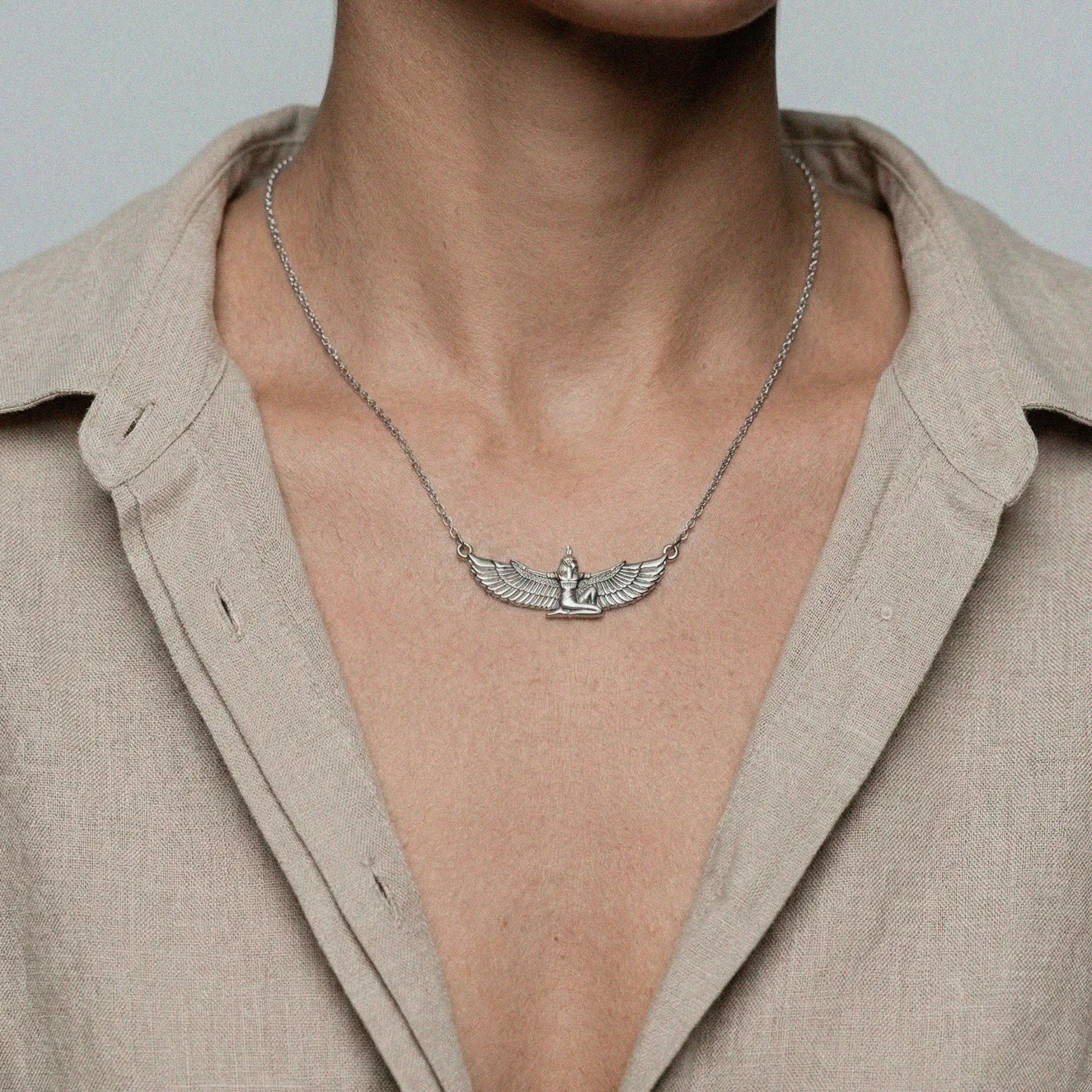 Necklace with an egyptian figure pendant worn by a person in a beige shirt.