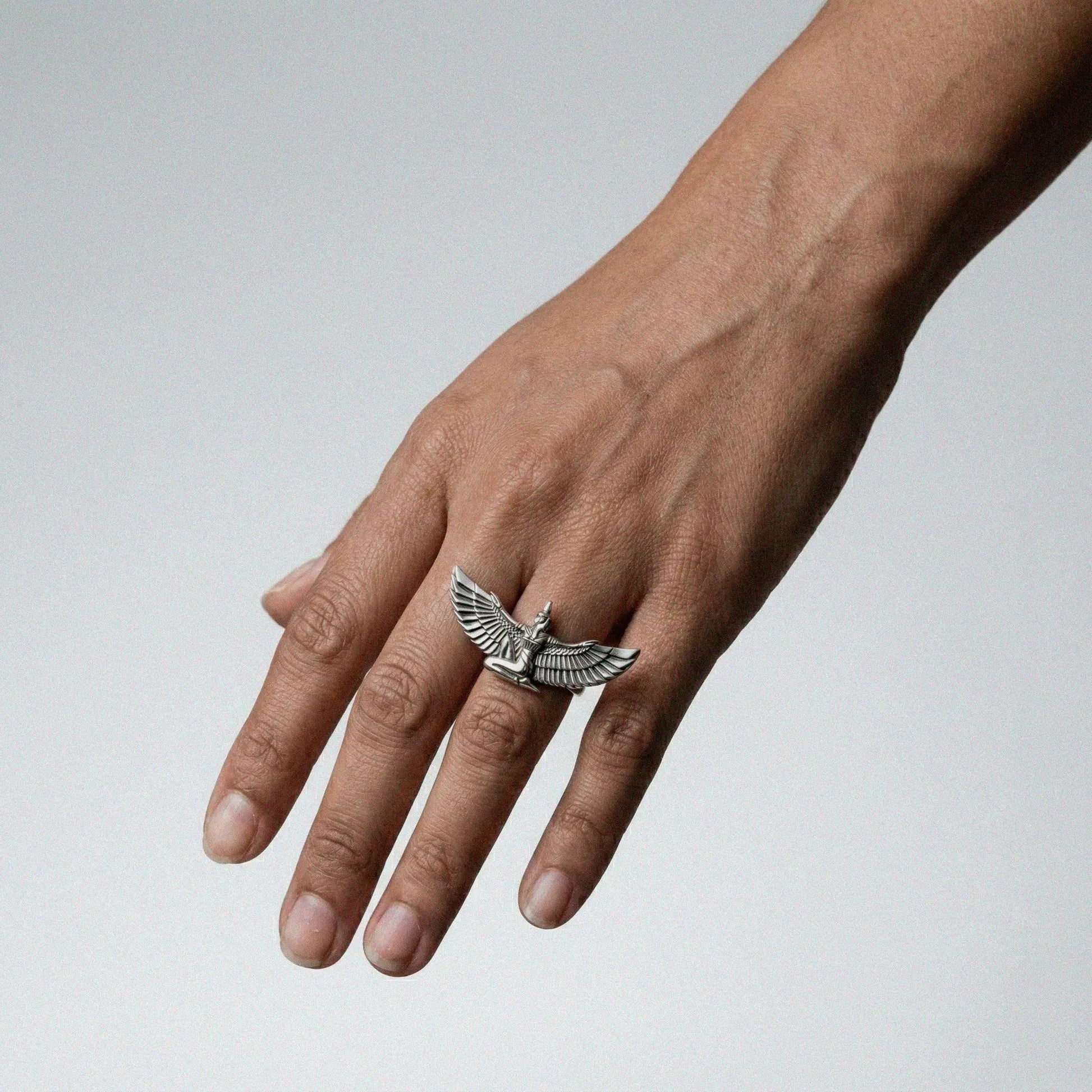 Hand wearing a silver ring with an isis design on a light gray background