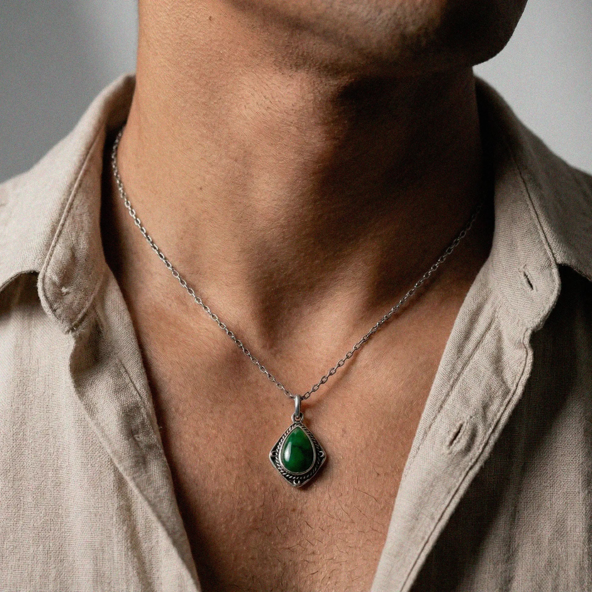 Necklace with a green jade stone pendant worn by a person wearing a beige shirt.