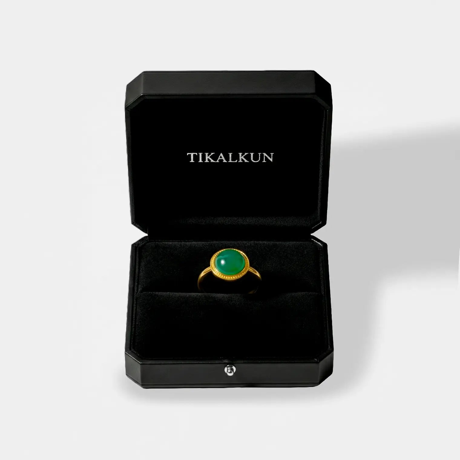 Gold ring with a jade gemstone in a black Tikalkun jewelry box on a light gray background