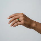 Hand wearing a ring with a jade gemstone on a plain background