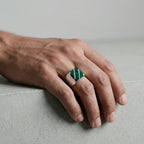 Hand wearing a green and white patterned ring on a neutral background