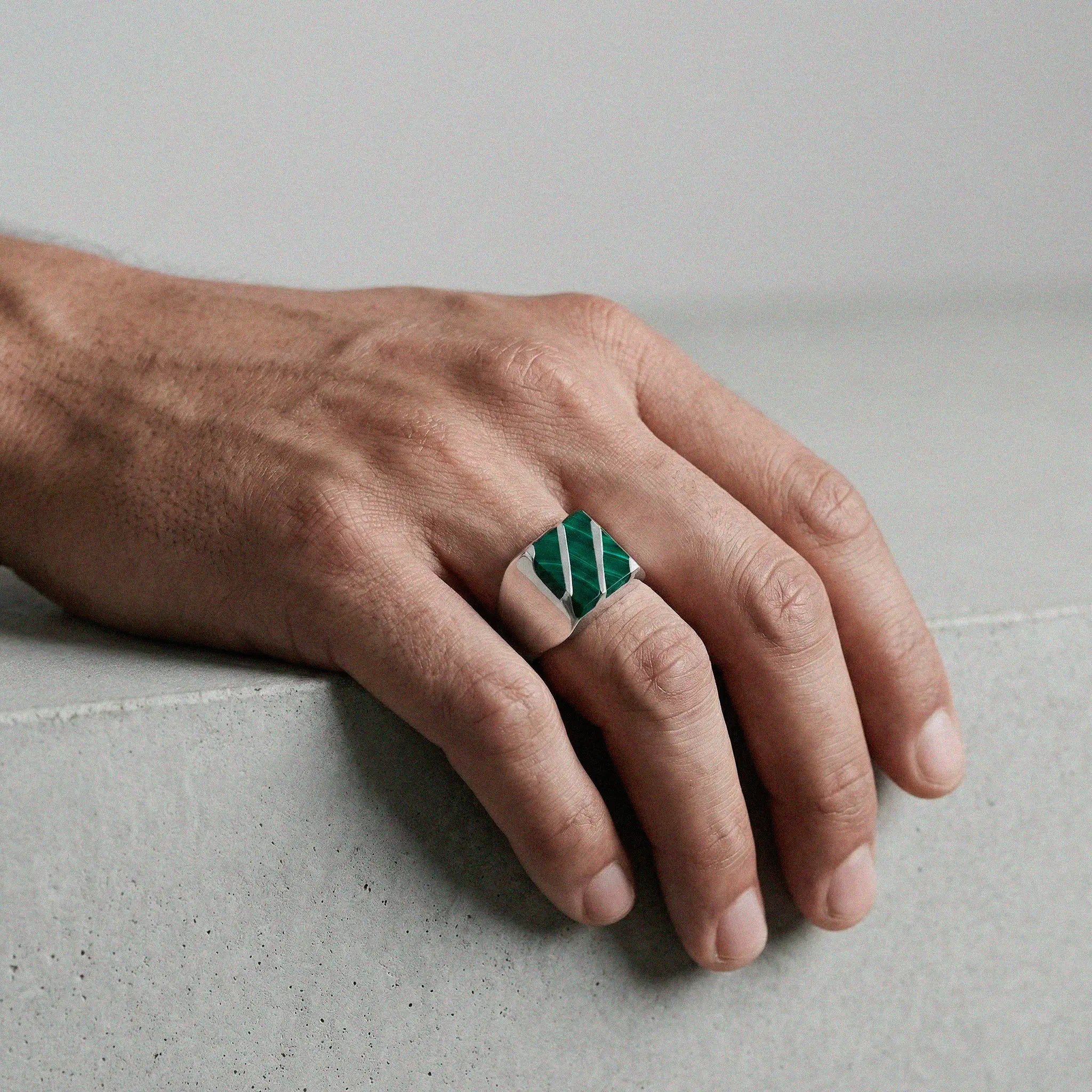 Hand wearing a green and white patterned ring on a neutral background
