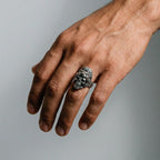 Hand wearing a silver jaguar-warrior skull ring on a gray background
