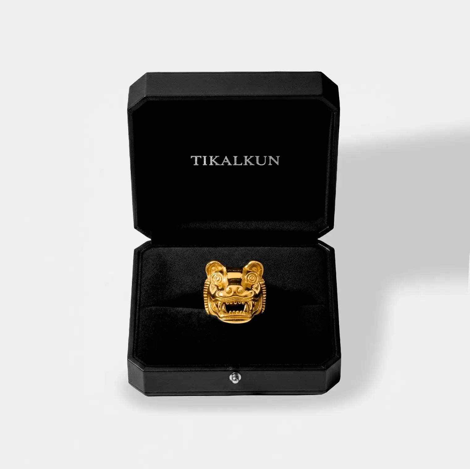 Gold jaguar head pendant in a black Tikalkun jewelry box on a light gray background