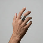 Hand wearing a silver ring with a knight's helmet design on a plain background