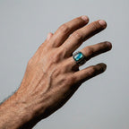 Hand wearing a ring with a labradorite gemstone on a gray background