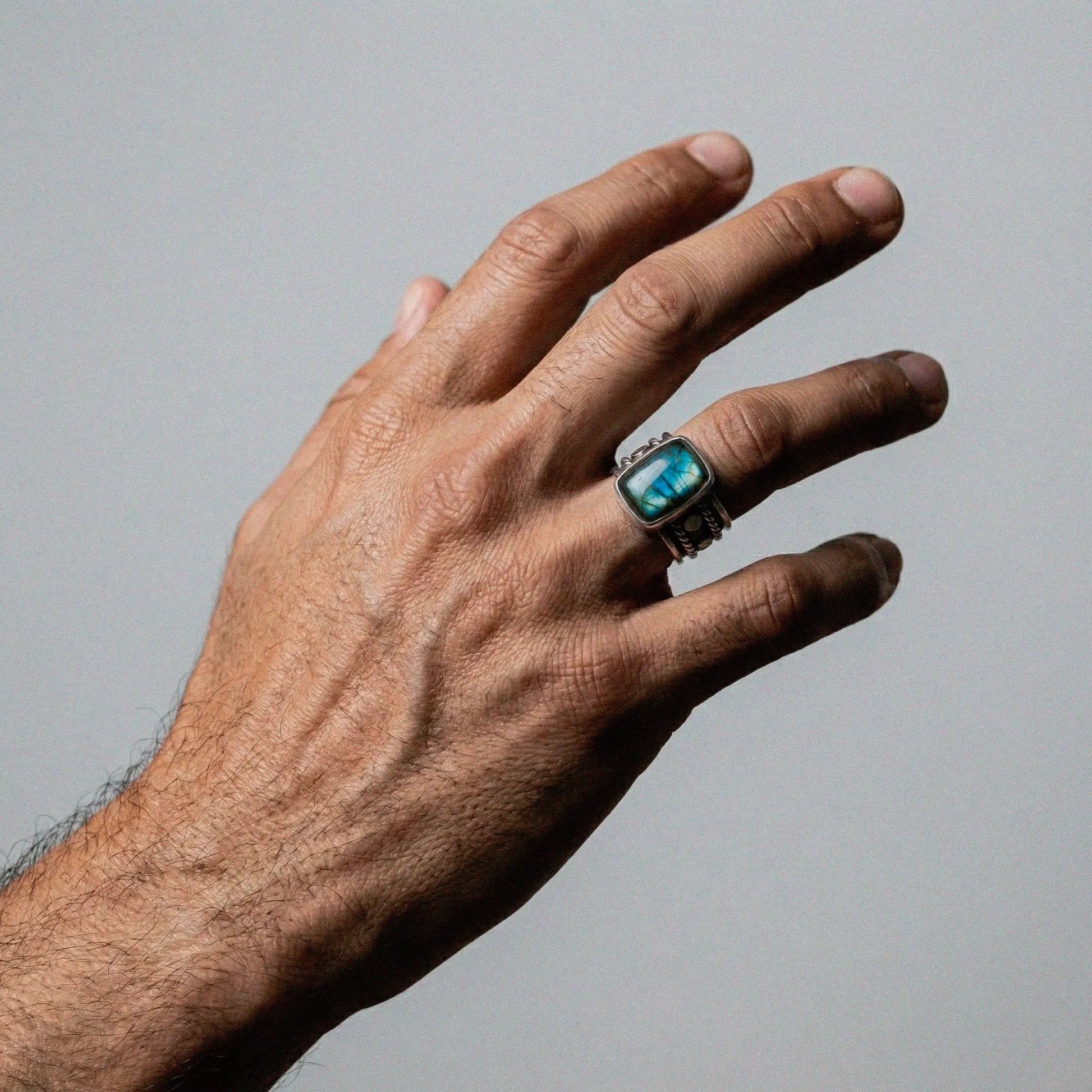 Hand wearing a ring with a labradorite gemstone on a gray background