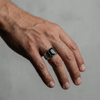 Hand wearing a silver ring with obsidian on a plain background