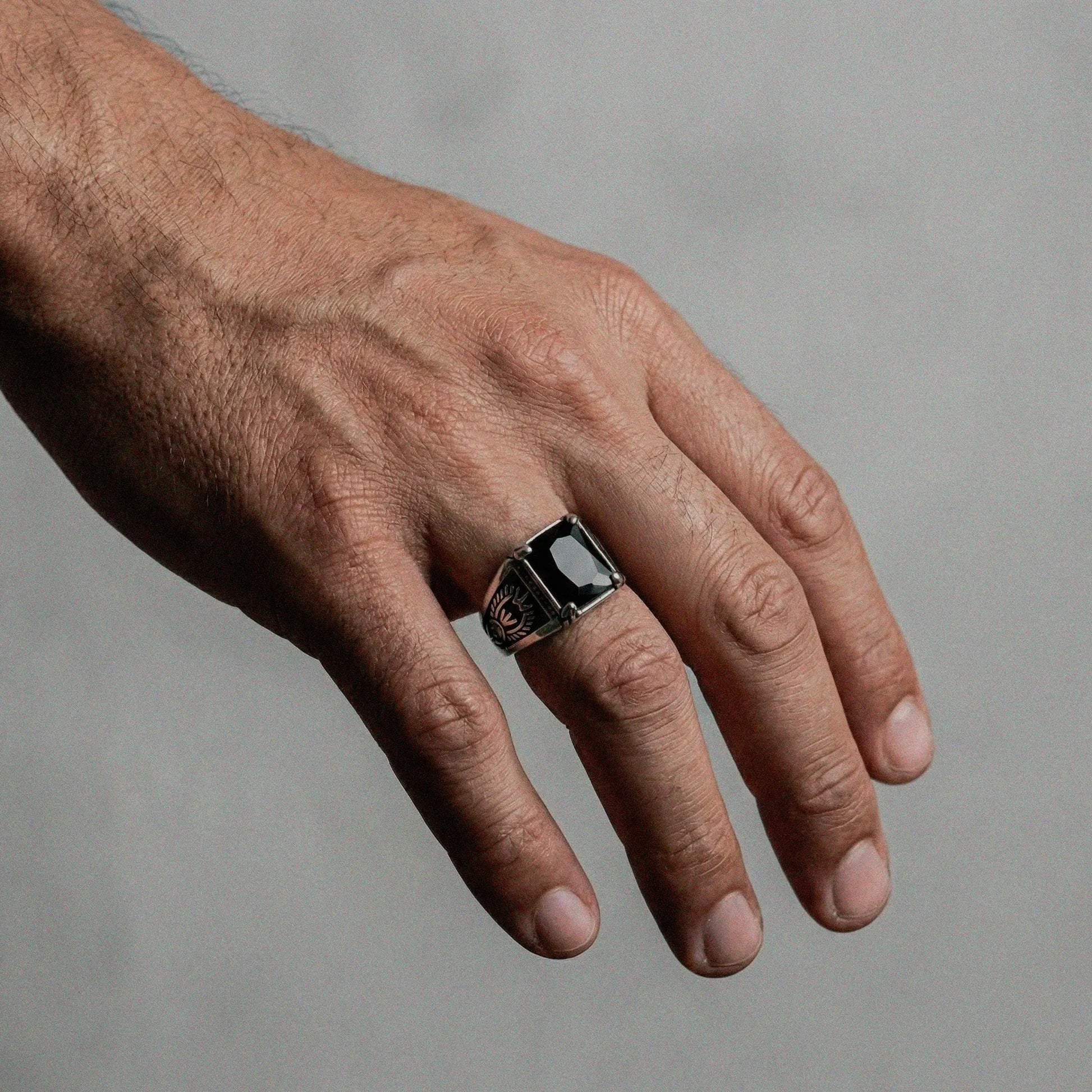 Hand wearing a silver ring with obsidian on a plain background