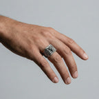 Hand wearing a silver lion head ring on a plain background