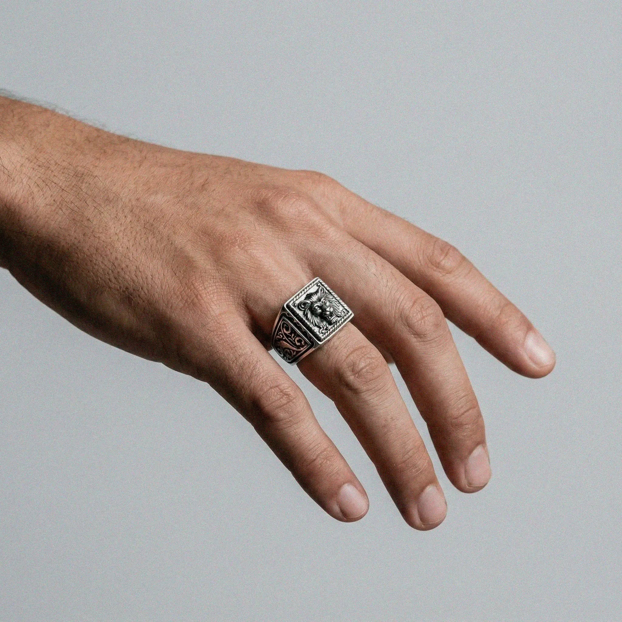 Hand wearing a silver lion head ring on a plain background