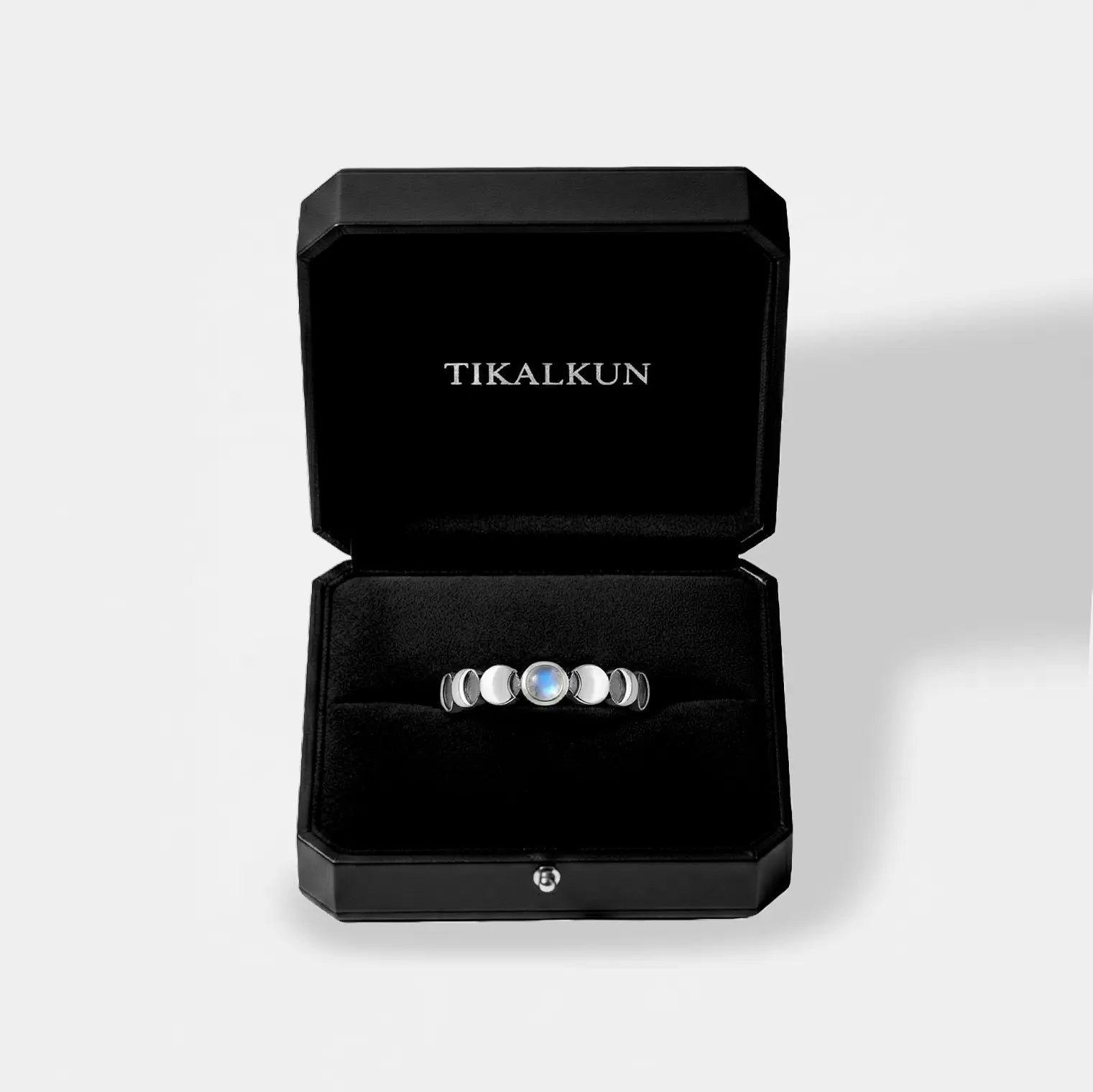 Black jewelry box with a lunar cycle ring inside, branded 'TIKALKUN', on a light gray background