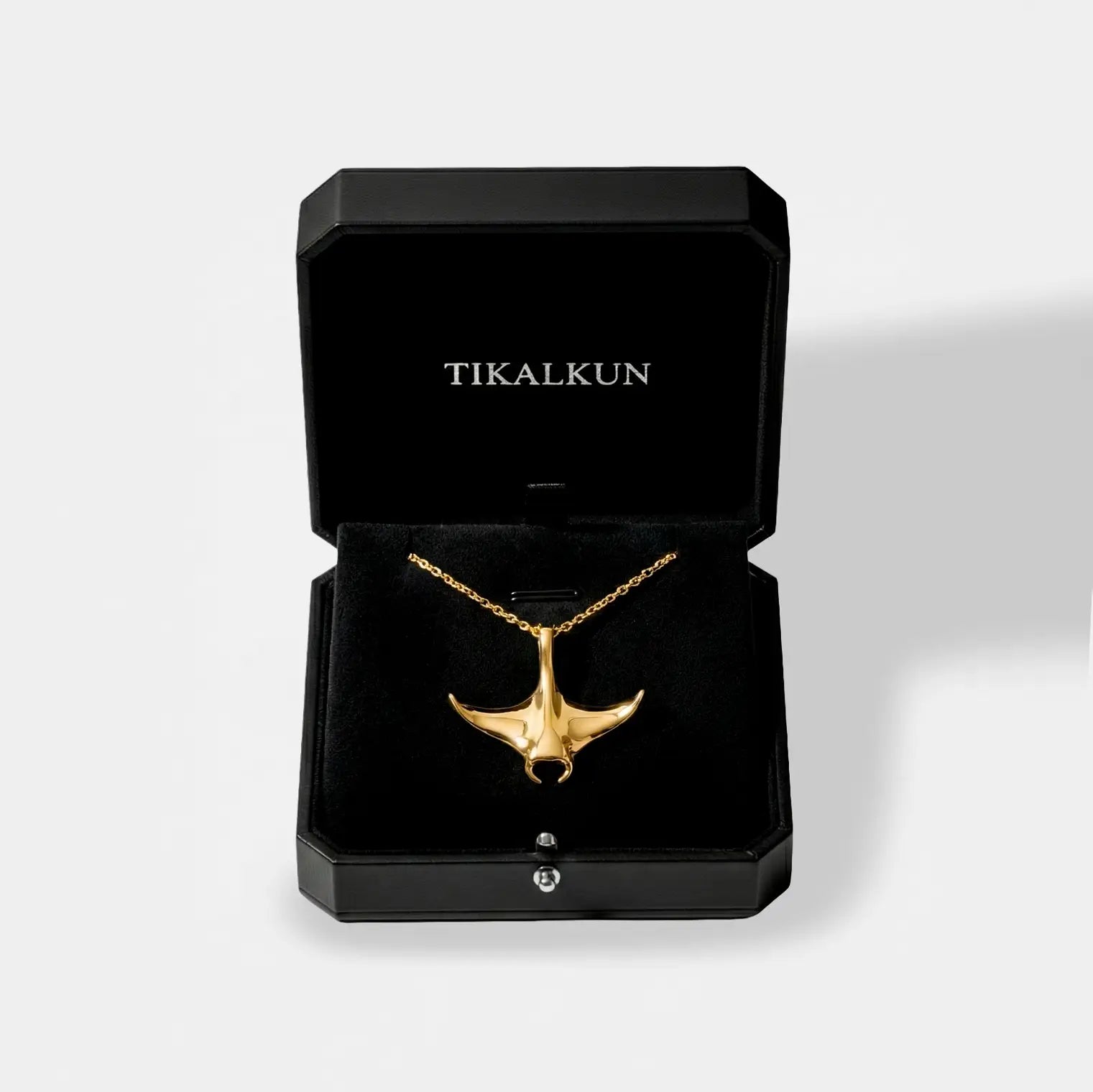 Gold manta ray necklace in a black Tikalkun jewelry box on a light gray background