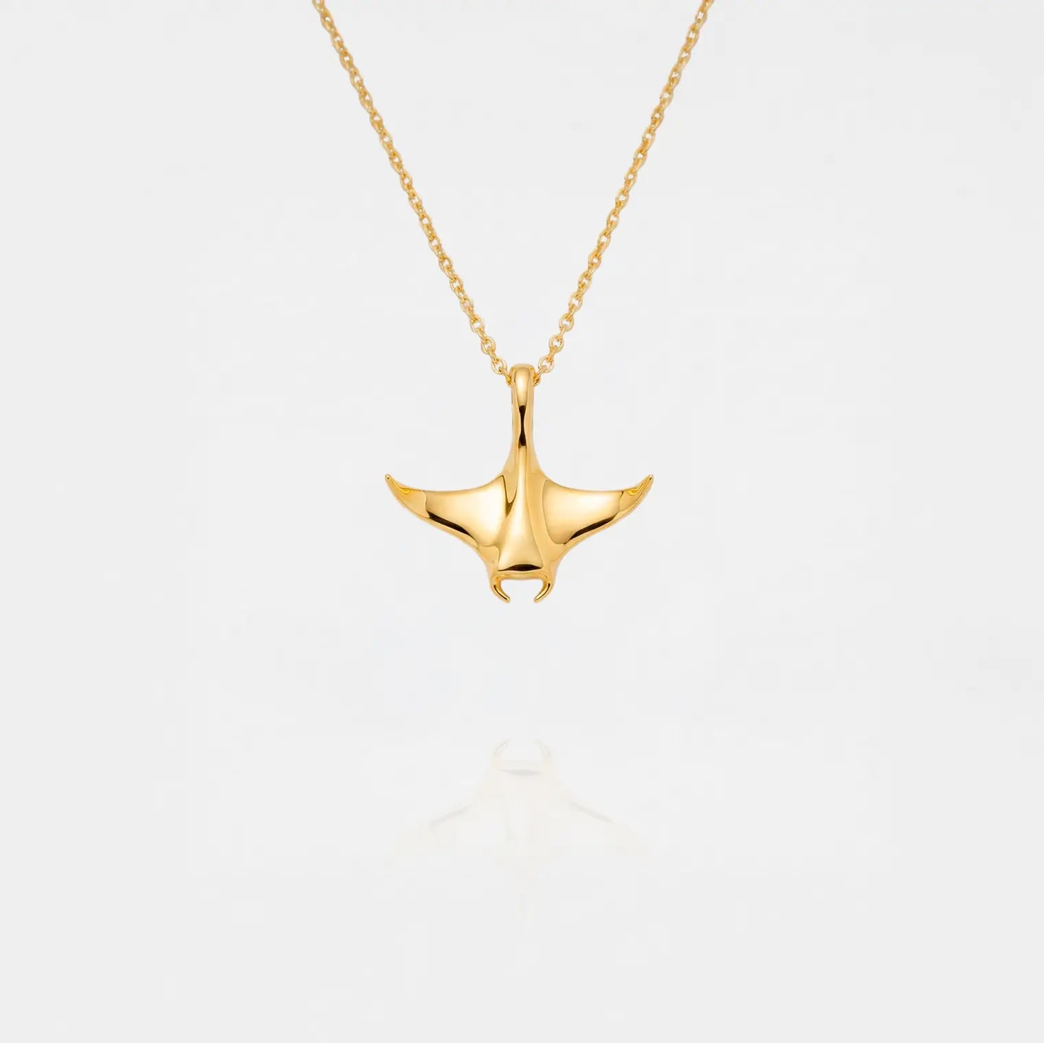 Gold MANTA RAY necklace on a light gray background
