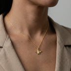 Gold necklace with a manta ray pendant worn by a person in a beige outfit.