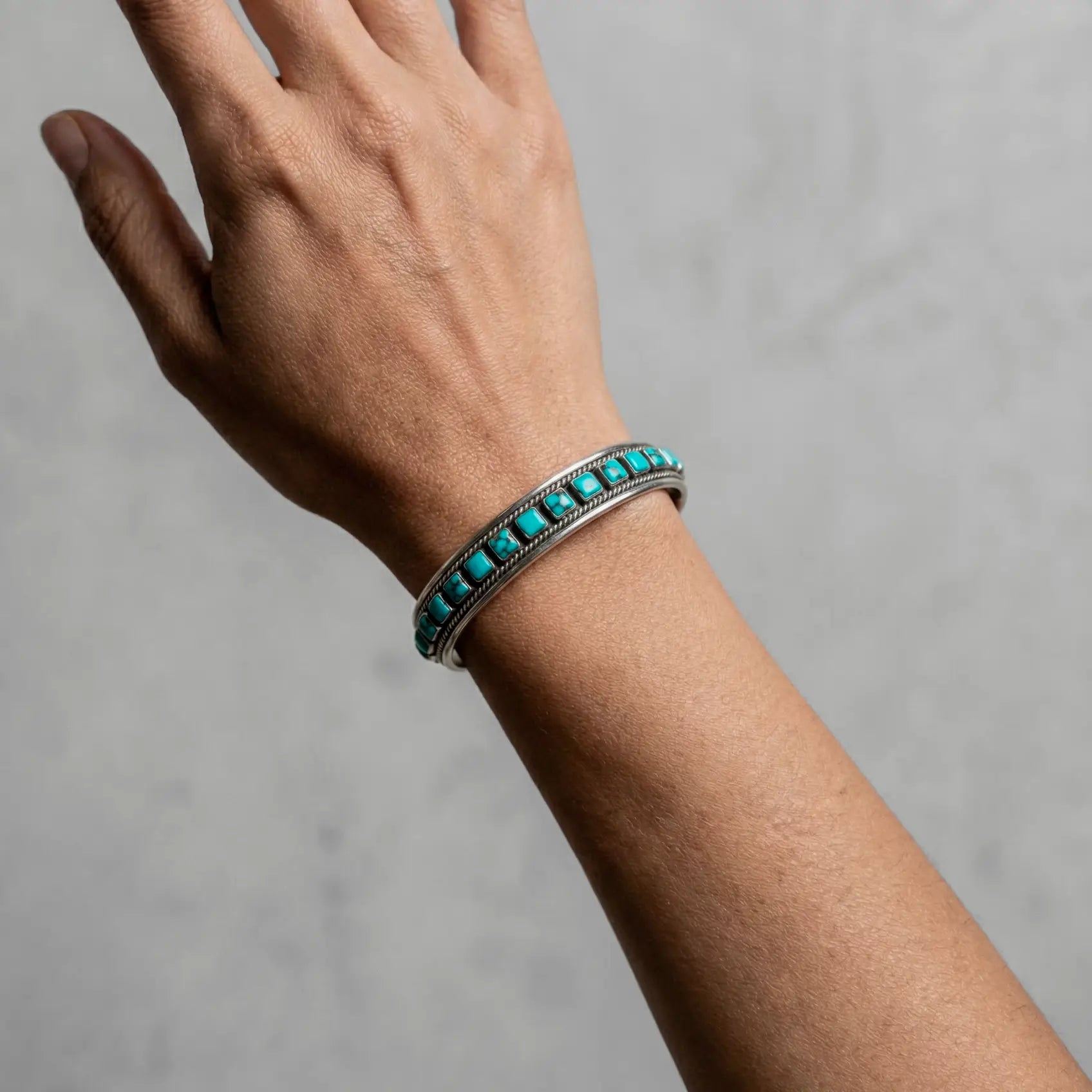 Hand wearing a turquoise beaded bracelet on a gray background