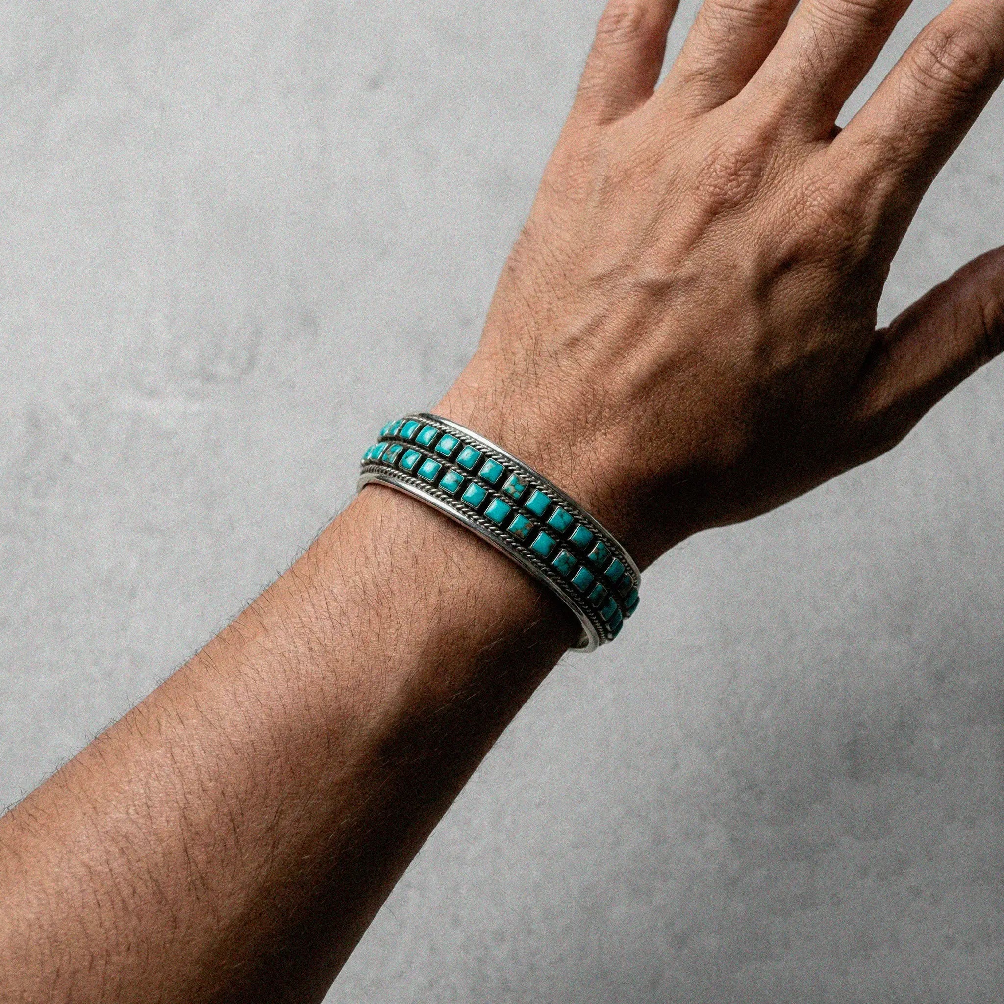 Hand wearing a turquoise beaded bracelet on a gray background