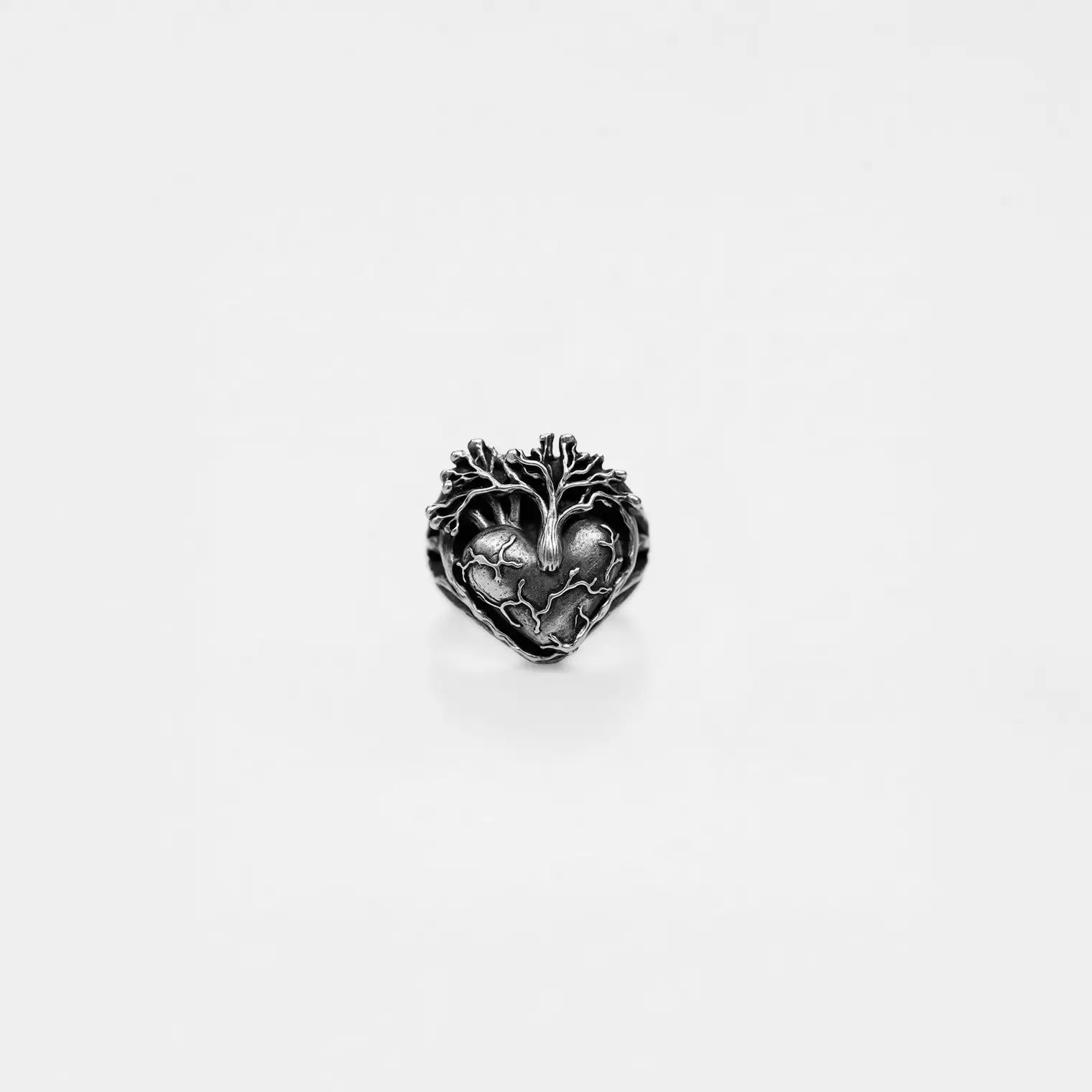 Silver heart-shaped jewelry piece with tree design on a white background